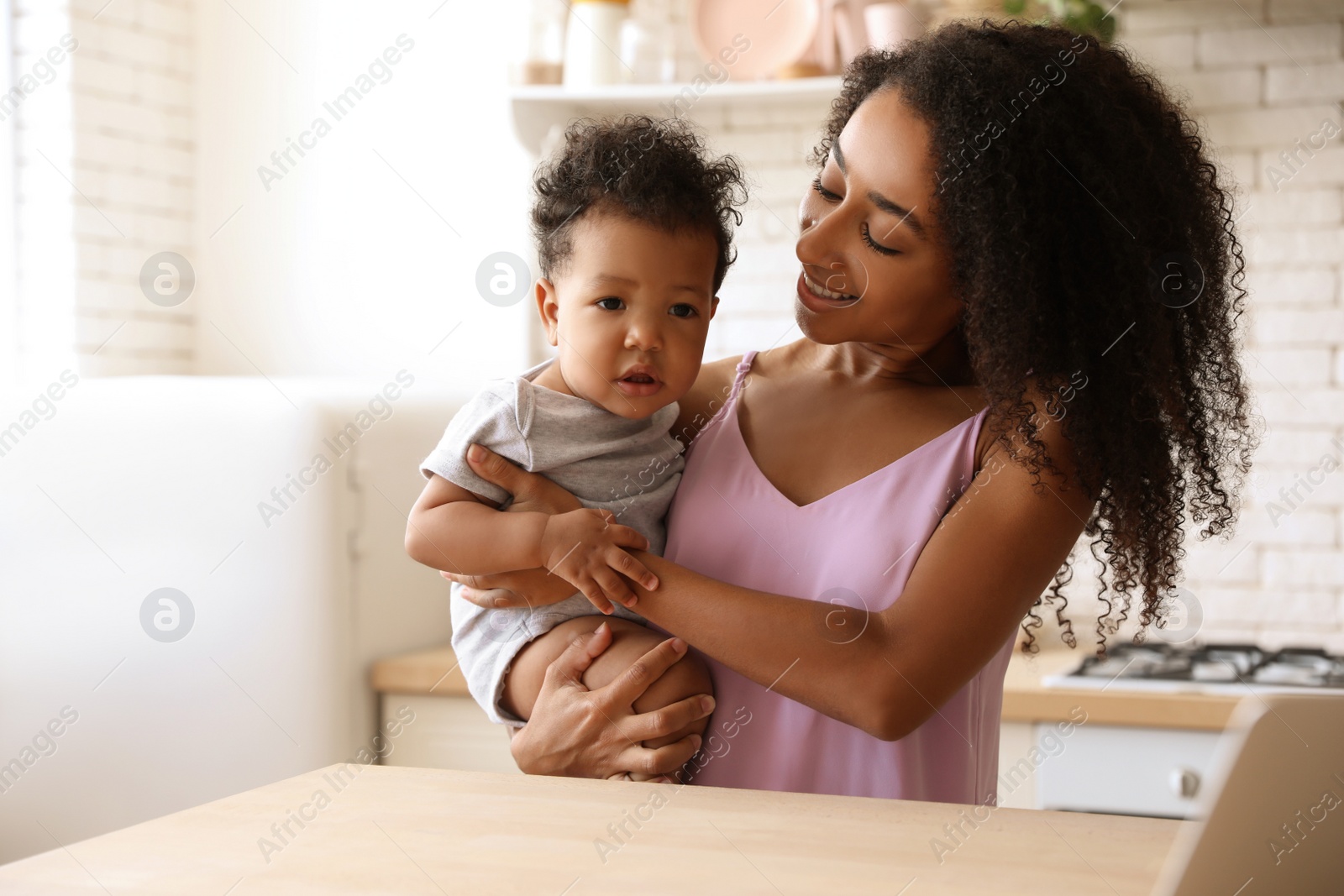 Photo of African-American woman with her baby in kitchen. Happiness of motherhood