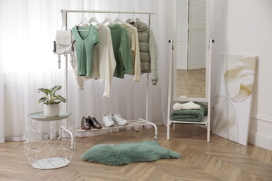 Photo of Rack with stylish warm clothes and shoes near mirror in dressing room