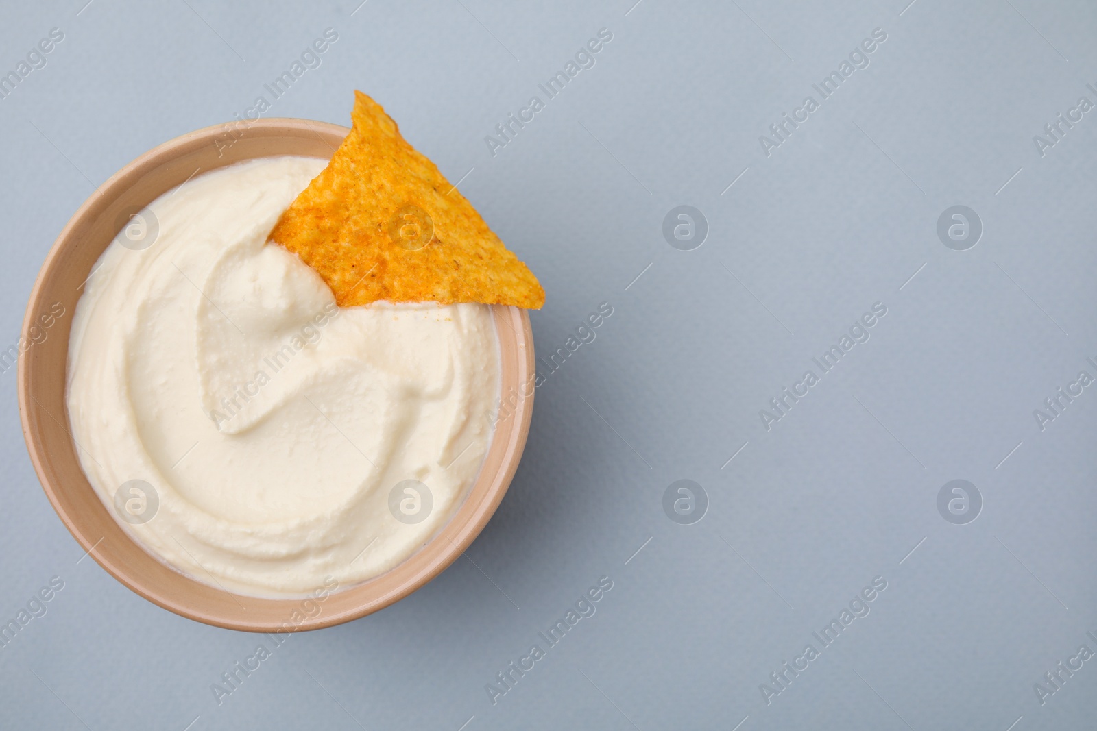 Photo of Delicious tofu sauce served with nachos chip in bowl on grey background, top view. Space for text