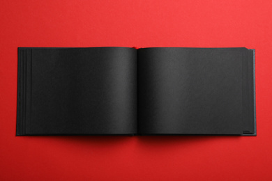Photo of Open black notebook on red background, top view