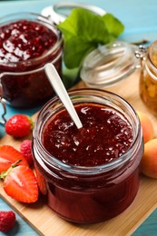 Jars with different jams and fresh fruits on light blue wooden table, closeup