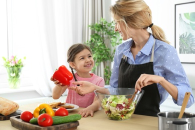 Young nanny with cute little girl cooking together in kitchen