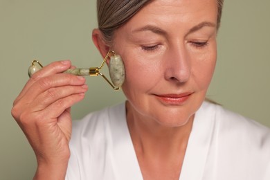 Photo of Woman massaging her face with jade roller on green background, closeup