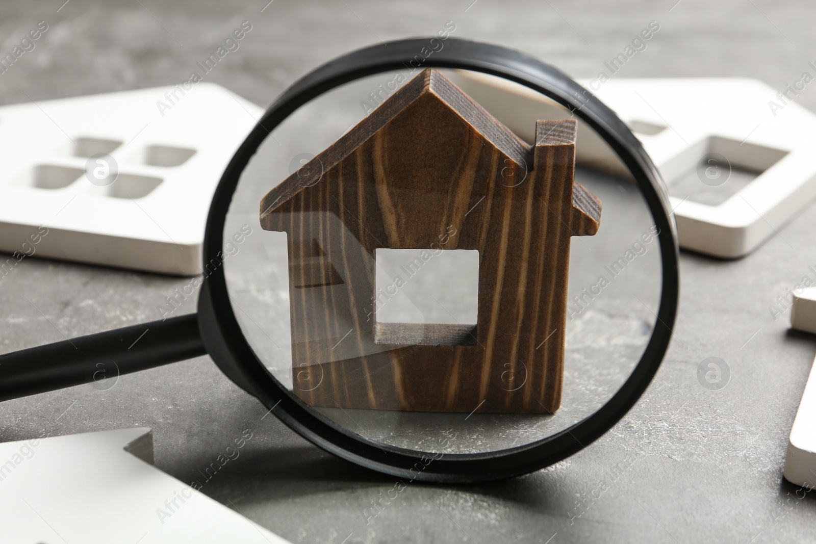 Photo of Magnifying glass and house models on grey stone table. Search concept