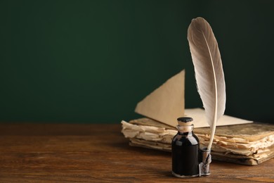 Photo of Feather pen, bottle of ink and old book on wooden table. Space for text