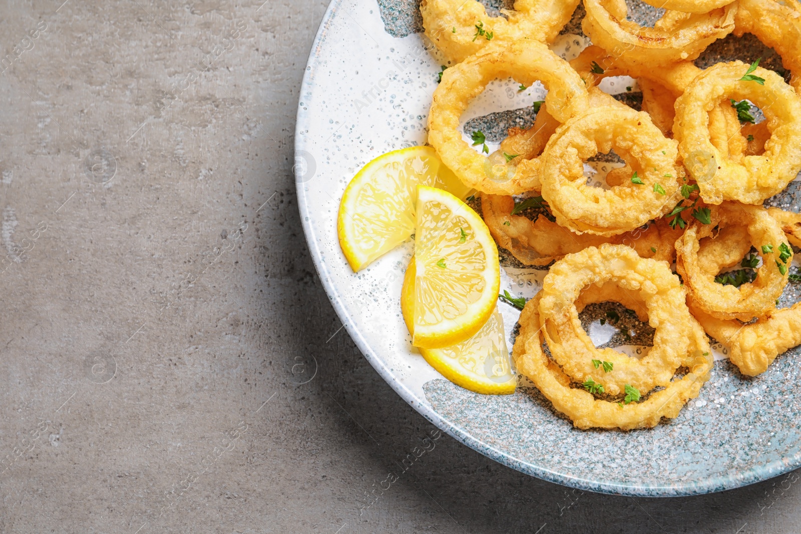Photo of Plate with homemade crunchy fried onion rings and lemon slices on gray background, top view. Space for text