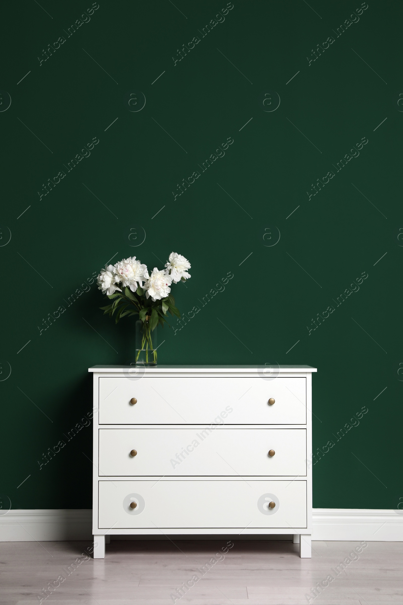Photo of Modern white chest of drawers with beautiful bouquet near green wall indoors