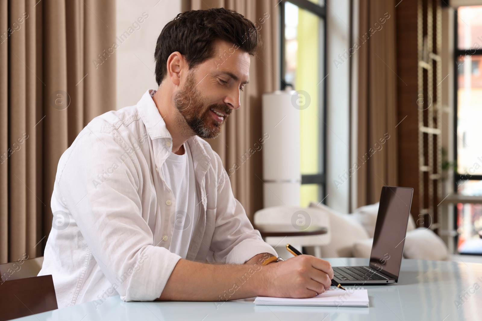 Photo of Man writing something and laptop at table in cafe