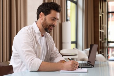 Man writing something and laptop at table in cafe