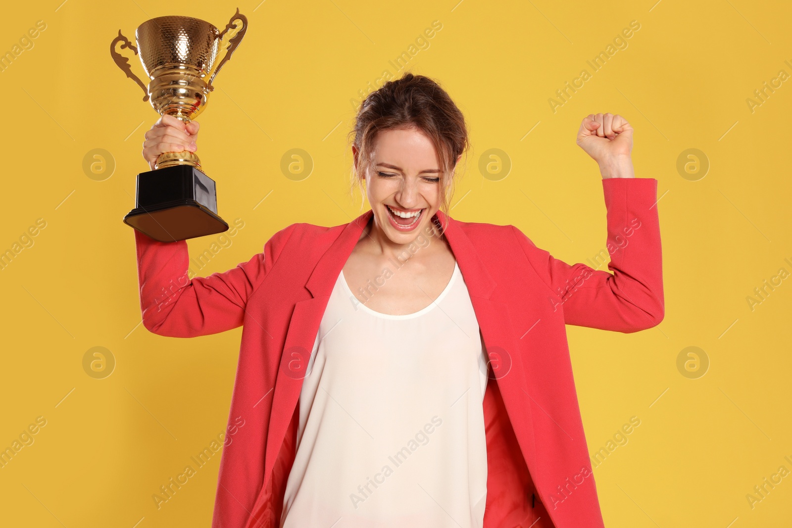 Photo of Portrait of happy young businesswoman with gold trophy cup on yellow background