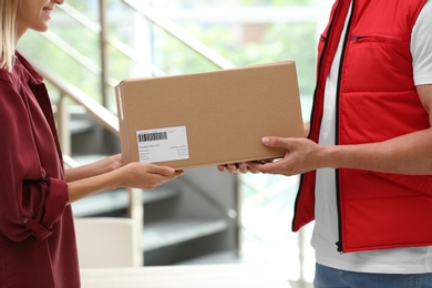 Photo of Woman receiving parcel from delivery service courier indoors