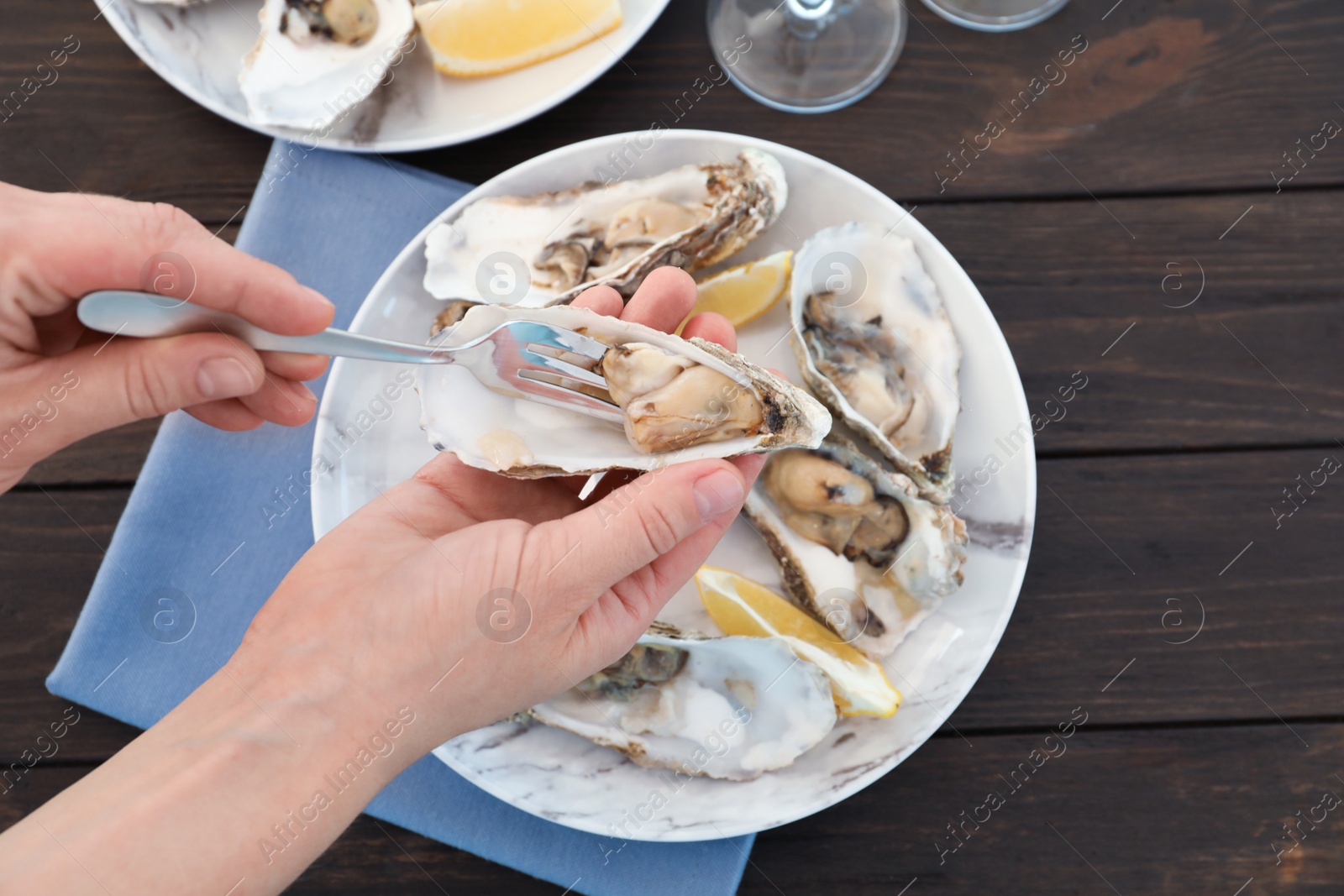 Photo of Top view of woman holding fresh oyster over plate at table