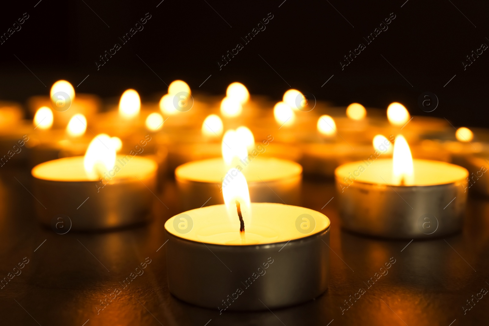 Photo of Burning candles on table in darkness, closeup. Funeral symbol