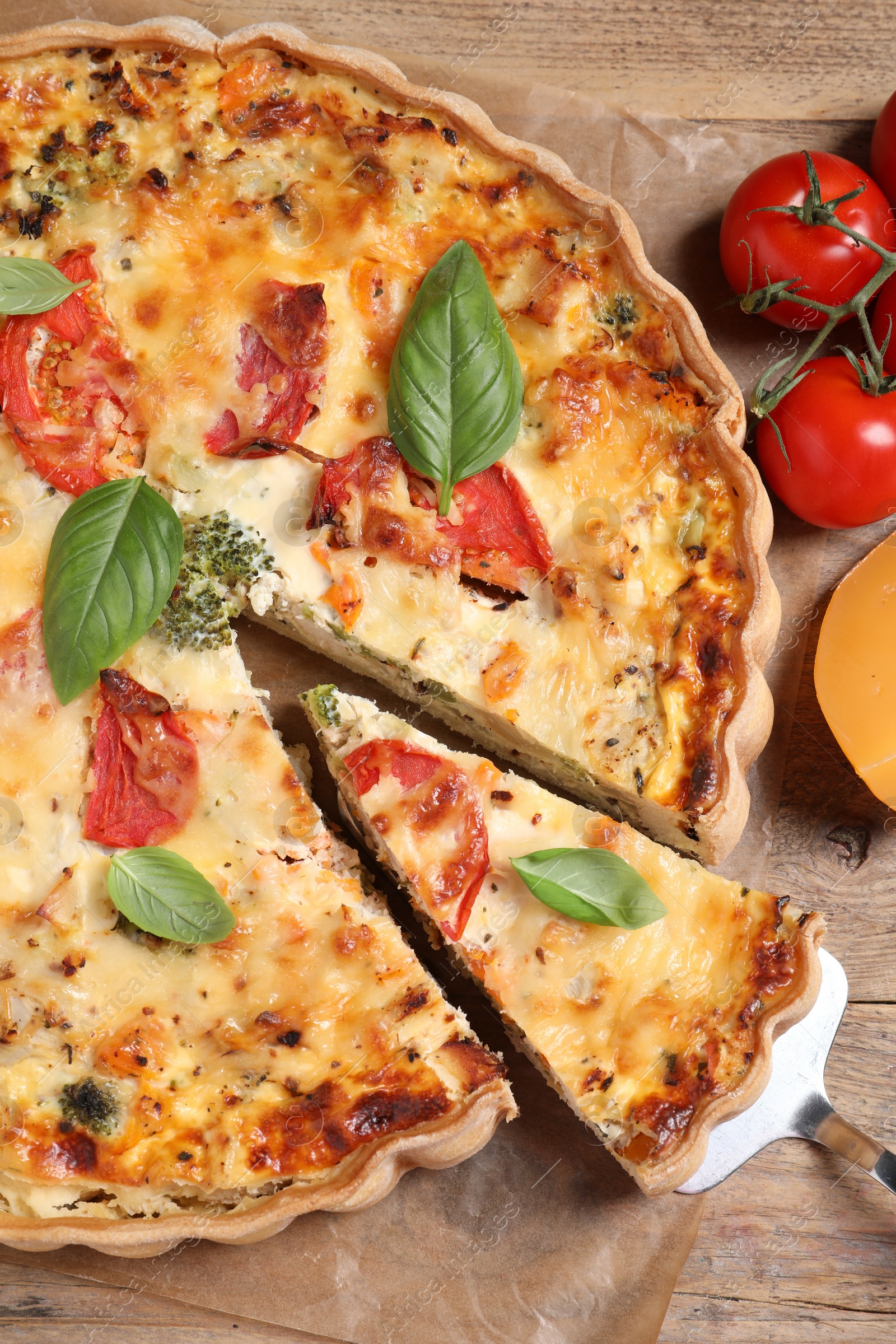 Photo of Tasty quiche with tomatoes, basil and cheese served on wooden table, flat lay