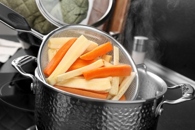 Putting cut parsnips and carrots into pot with boiling water in kitchen, closeup