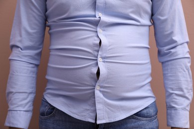 Man wearing tight shirt on pale pink background, closeup. Overweight problem