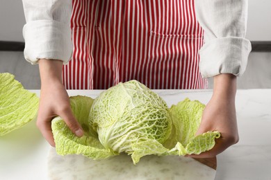 Photo of Woman separating leaf from fresh savoy cabbage at white marble table, closeup