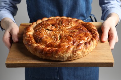 Photo of Woman holding tasty homemade pie on light grey background, closeup