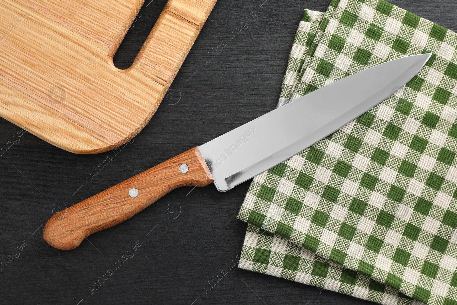 Photo of One sharp knife, napkin and board on black wooden table, flat lay