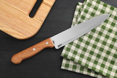 Photo of One sharp knife, napkin and board on black wooden table, flat lay