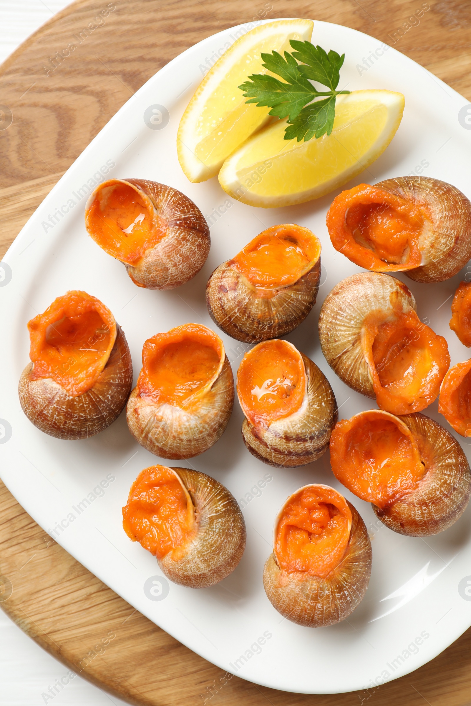 Photo of Delicious cooked snails with lemon and parsley on white table, top view