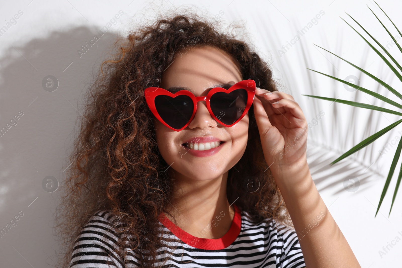 Photo of Young beautiful African-American woman wearing heart shaped glasses and tropical palm leaf on white background