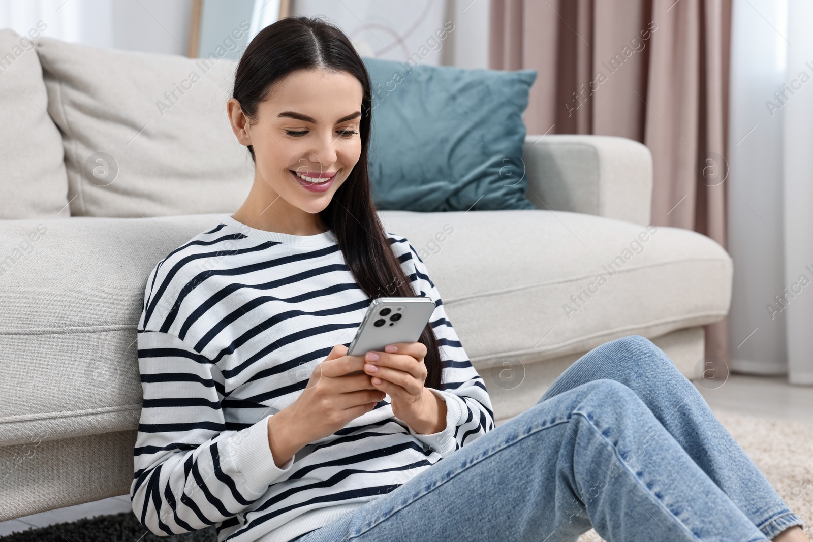 Photo of Happy young woman using smartphone at home