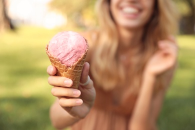 Photo of Happy young woman with delicious ice cream in waffle cone outdoors, focus on hand