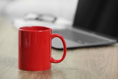 Photo of Red ceramic mug and laptop on wooden table indoors. Space for text