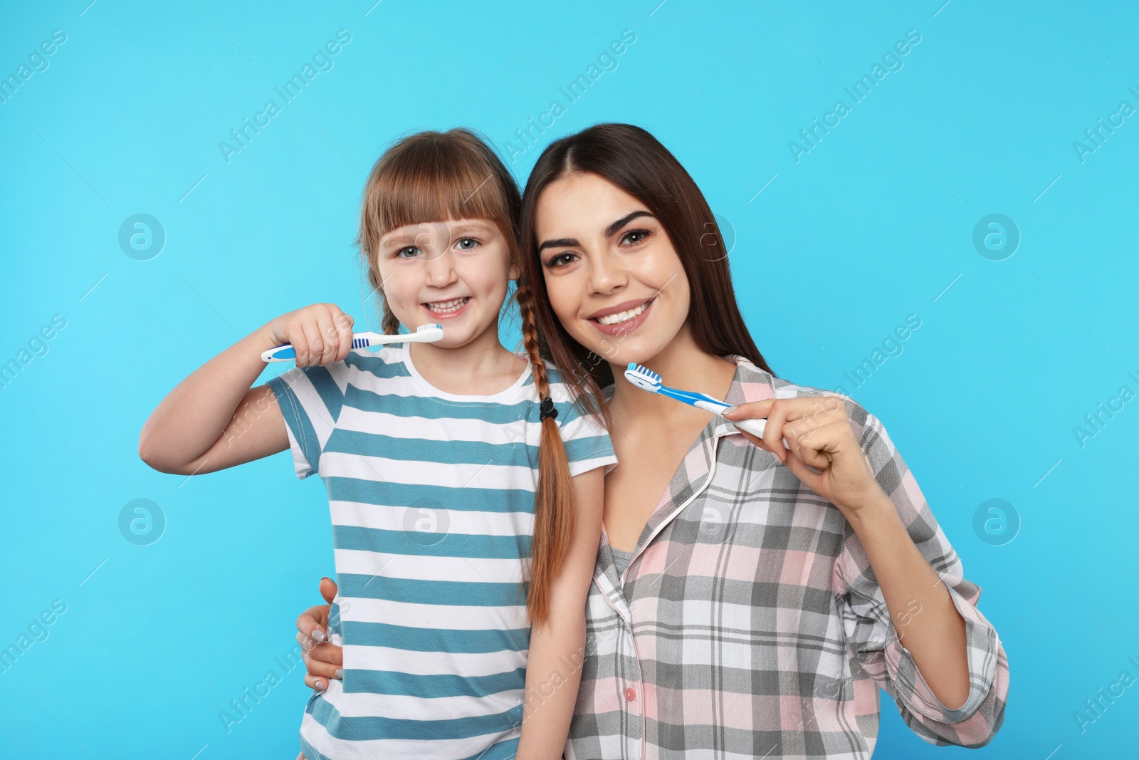 Photo of Little girl and her mother brushing teeth together on color background