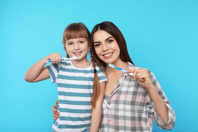 Little girl and her mother brushing teeth together on color background