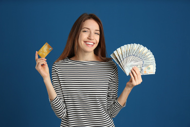 Happy young woman with cash money and credit card on blue background