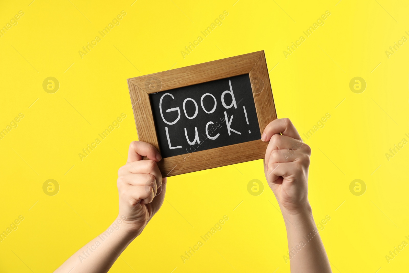 Photo of Woman holding blackboard with words GOOD LUCK on yellow background, closeup