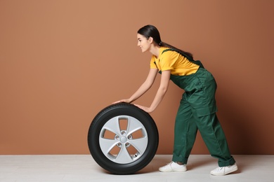 Photo of Female mechanic in uniform with car tire on color wall background