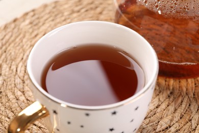 Photo of Aromatic tea in cup on wicker mat, closeup