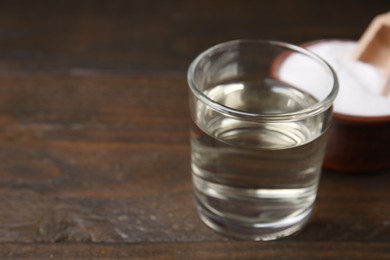 Photo of Vinegar in glass and baking soda on wooden table, closeup. Space for text