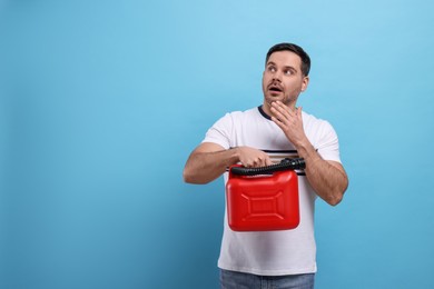 Emotional man holding red canister on light blue background, space for text