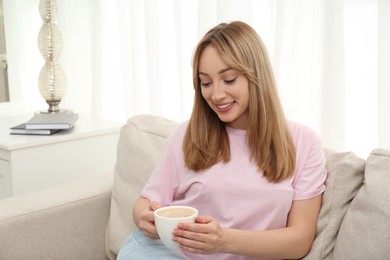 Photo of Beautiful young woman with cup of coffee relaxing on sofa at home