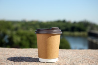 Photo of Takeaway cardboard coffee cup with plastic lid on stone surface outdoors