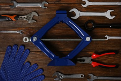 Photo of Car scissor jack, gloves and different tools on wooden surface, flat lay