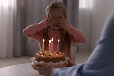 Photo of Birthday celebration. Mother holding tasty cake with burning candles near her daughter indoors