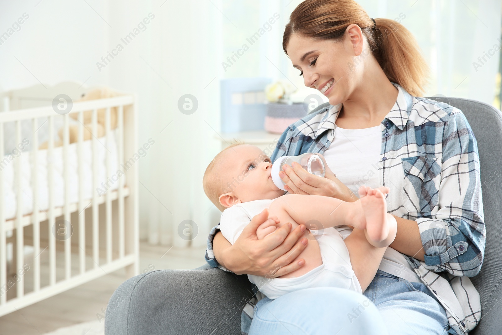 Photo of Lovely mother giving her baby drink from bottle in room. Space for text