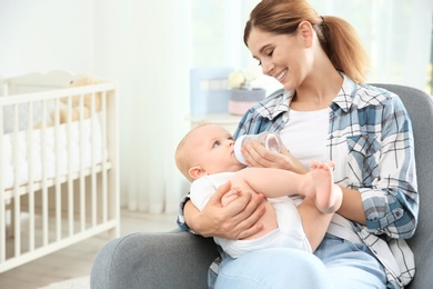 Photo of Lovely mother giving her baby drink from bottle in room. Space for text