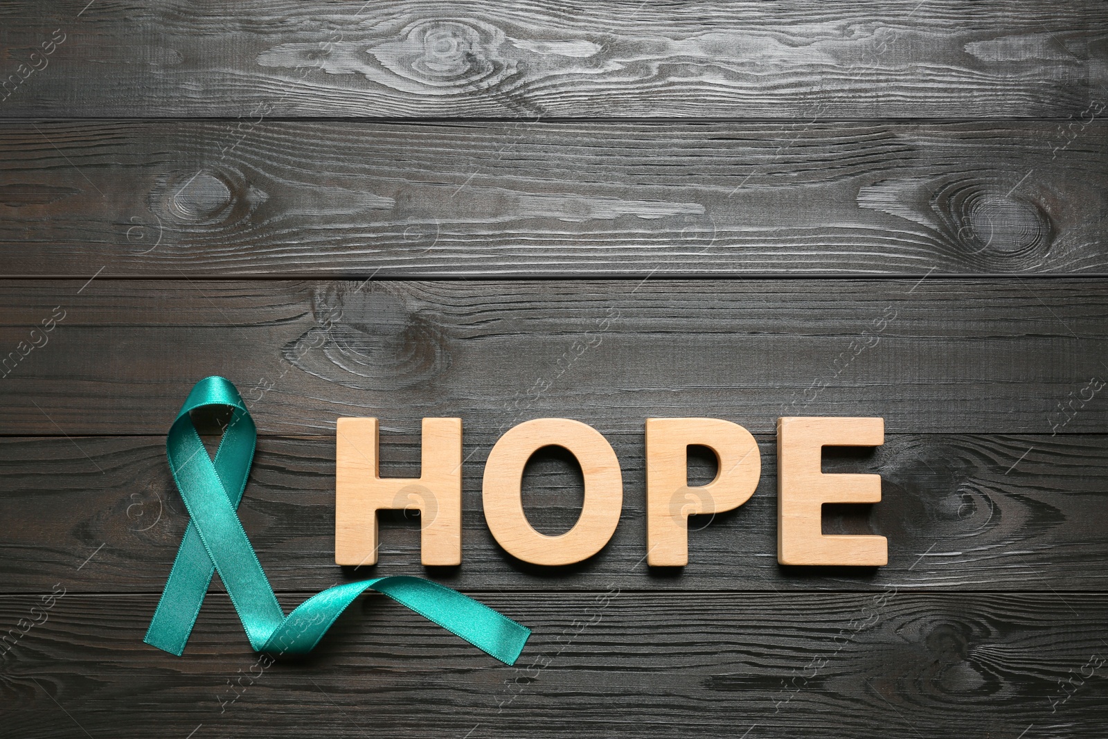Photo of Word Hope made of letters and teal awareness ribbon on wooden background, top view. Symbol of social and medical issues