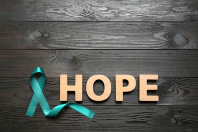 Photo of Word Hope made of letters and teal awareness ribbon on wooden background, top view. Symbol of social and medical issues