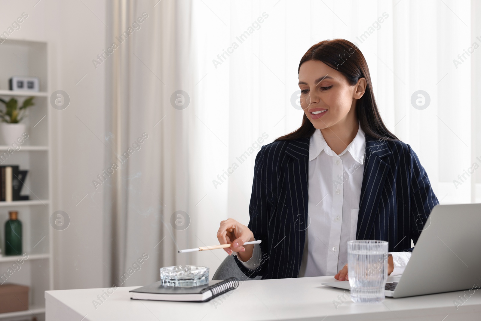 Photo of Woman using long cigarette holder for smoking at workplace in office