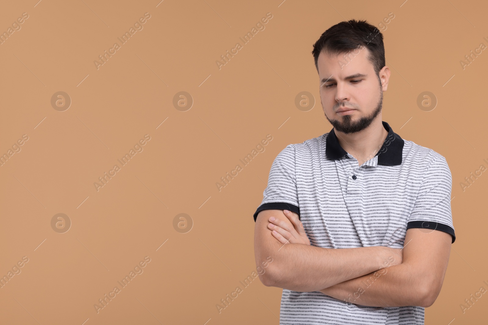 Photo of Portrait of sad man with crossed arms on beige background, space for text