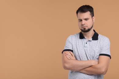 Portrait of sad man with crossed arms on beige background, space for text