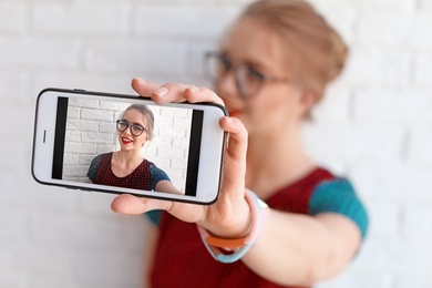 Photo of Attractive young woman taking selfie near brick wall, closeup