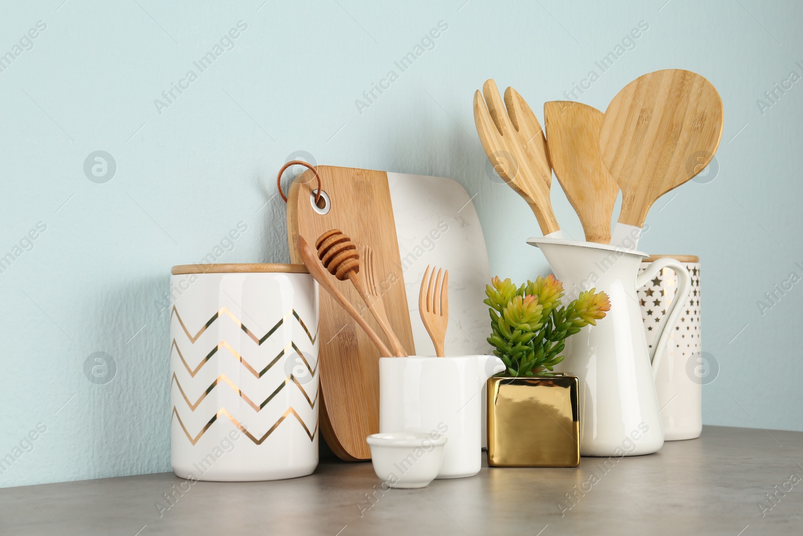 Photo of Potted plant and set of kitchenware on grey table near light wall. Modern interior design